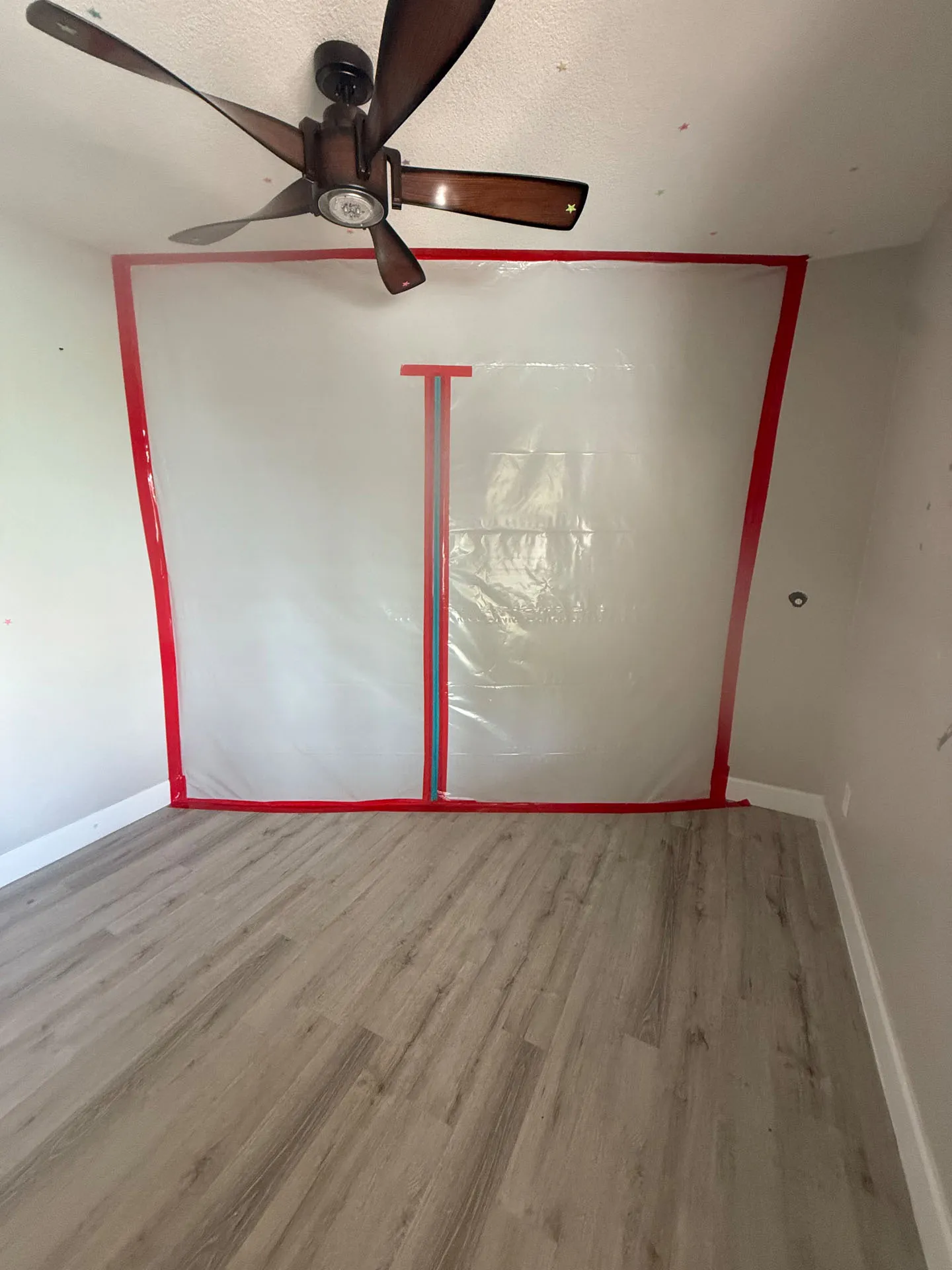 Plastic sheeting barrier with red tape seals off a construction zone in a room with laminate floors.