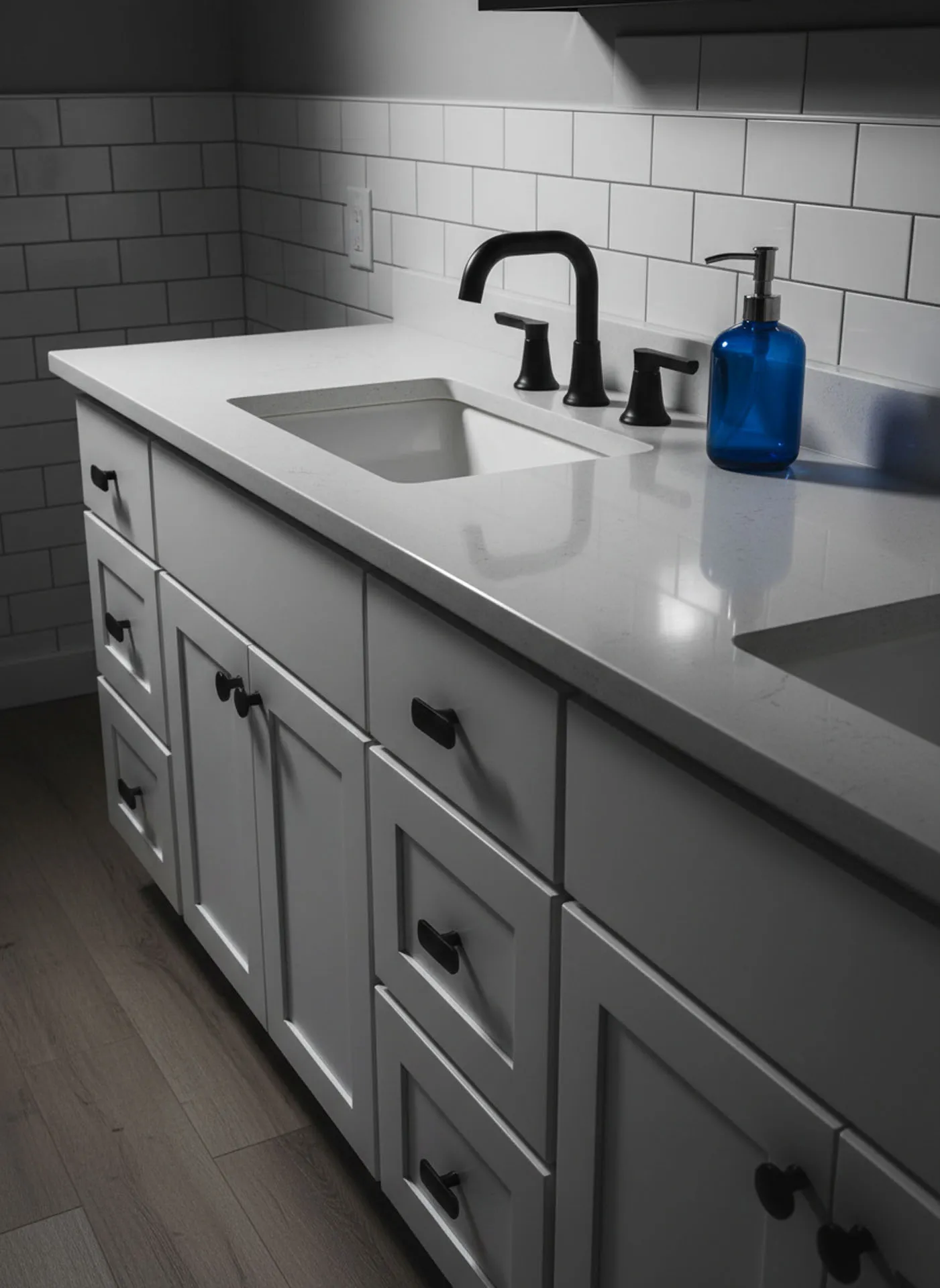 White shaker bathroom vanity featuring a quartz countertop, matte black faucet, and white subway tile backsplash.